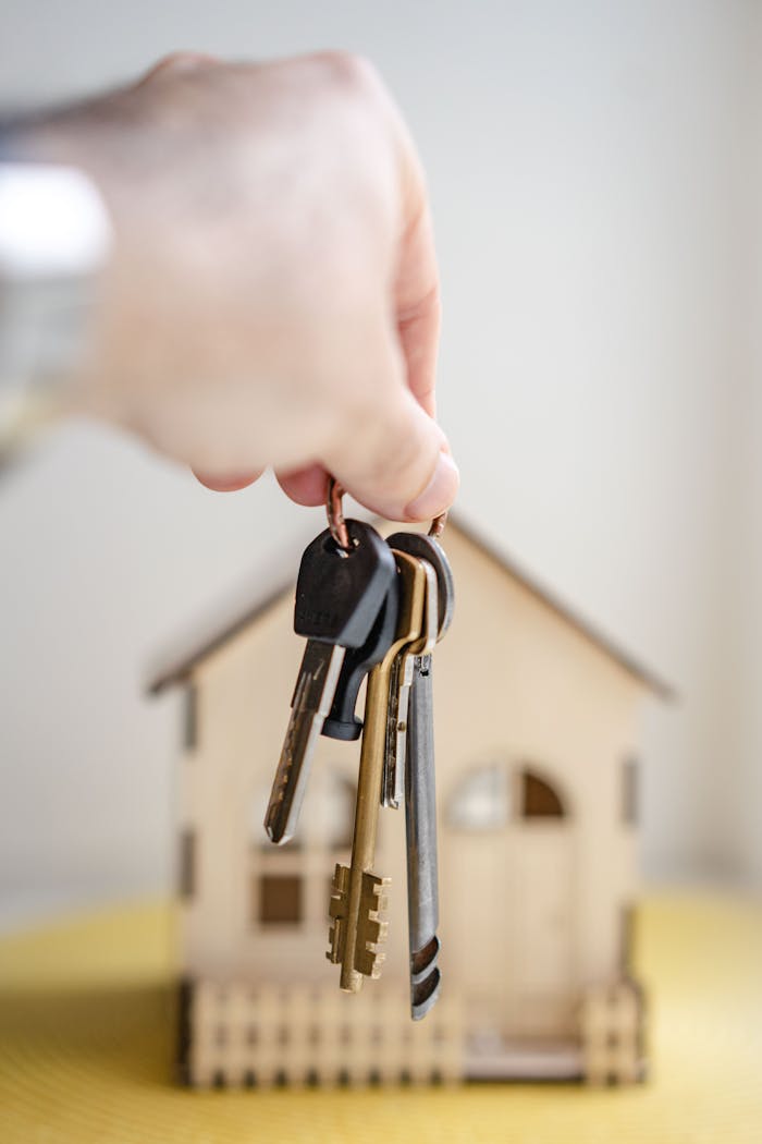 why-choose-us Close-up of a hand holding keys with a miniature wooden house in the background, symbolizing real estate investment.