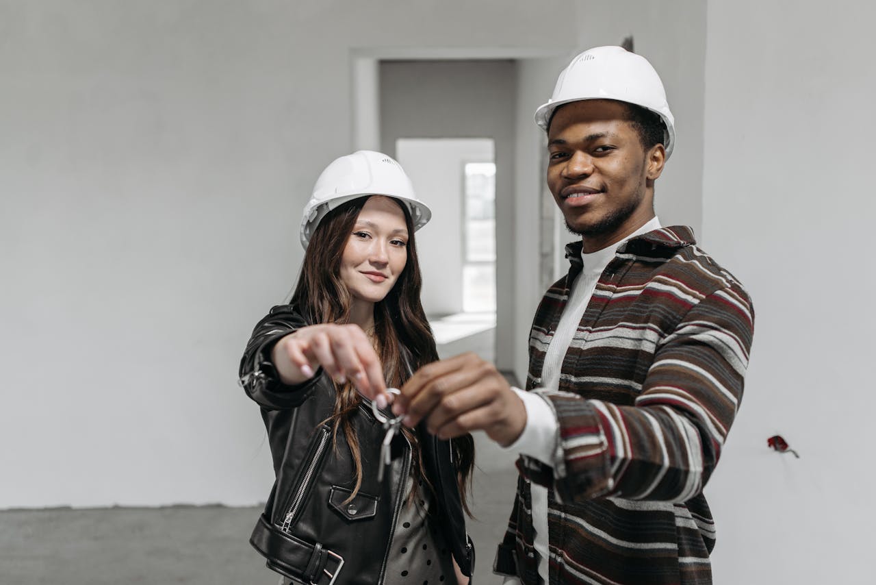 Mastering the First Impression: Your intriguing post title goes here A happy couple holding keys in a newly bought house, wearing white helmets.